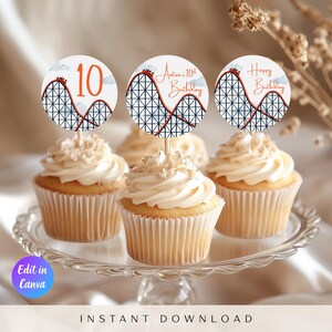 Könnte beinhalten: Cupcakes mit weißem Zuckerguss und dekorativen Toppern. Die Topper zeigen ein Achterbahn-Design mit der Zahl 10, dem Text "Anton's 10th Birthday" und "Happy Birthday". Die Cupcakes stehen auf einer Glas-Kuchenplatte.