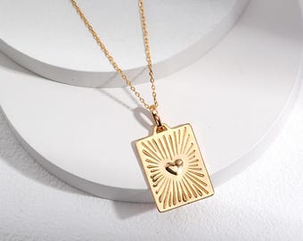 May include: A gold chain necklace with a rectangular pendant featuring a sunburst design and a small heart in the center.