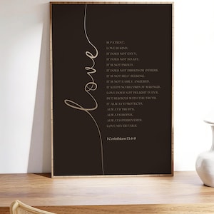 Op de afbeelding: Een rechthoekig ingelijst wandkunstwerk met een donkerbruine achtergrond en het woord love in een groot, lichtgekleurd cursief handschrift. De tekst bevat het volledige bijbelgedeelte uit 1 Korintiërs 13:4-8 in een strak lettertype.