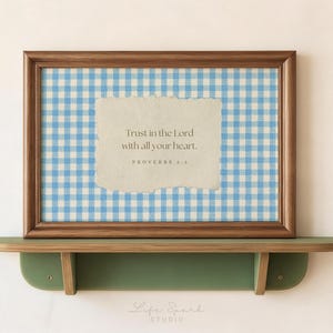 May include: A rectangular wooden frame containing a print with a light blue and white gingham pattern. Centered on the print is a cream-colored paper cutout with the text: Trust in the Lord with all your heart. PROVERBS 3:5.