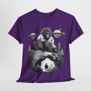 May include: Purple t-shirt with a black and white graphic of a gorilla sitting on a globe with flying saucers and buildings in the background.