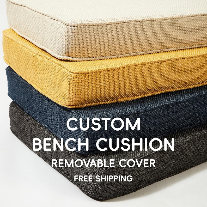 Op de afbeelding: Een stapel op maat gemaakte bankkussens in verschillende kleuren: cr&egrave;me, beige, mosterdgeel, marineblauw en antracietgrijs. De kussens hebben een textuurstof en de tekst "CUSTOM BENCH CUSHION REMOVABLE COVER".