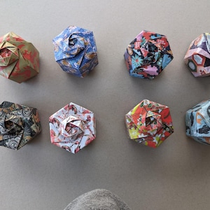 Pode incluir: Oito caixas de origami com diferentes padrões florais. As caixas são hexagonais e têm um centro elevado. Os padrões incluem vermelho, azul, verde, amarelo e branco.