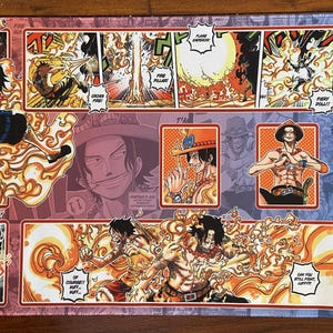May include: A rectangular playmat featuring a colorful manga-style illustration. The design showcases a character surrounded by flames, with panels of action scenes and text bubbles. The color palette includes red, orange, and blue.