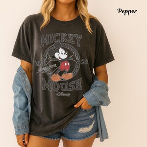 May include: Dark grey t-shirt with a distressed Mickey Mouse graphic, the text "Mickey Mouse" and "1928". The shirt has short sleeves and a crew neck. The word "Disney" is printed below the graphic.