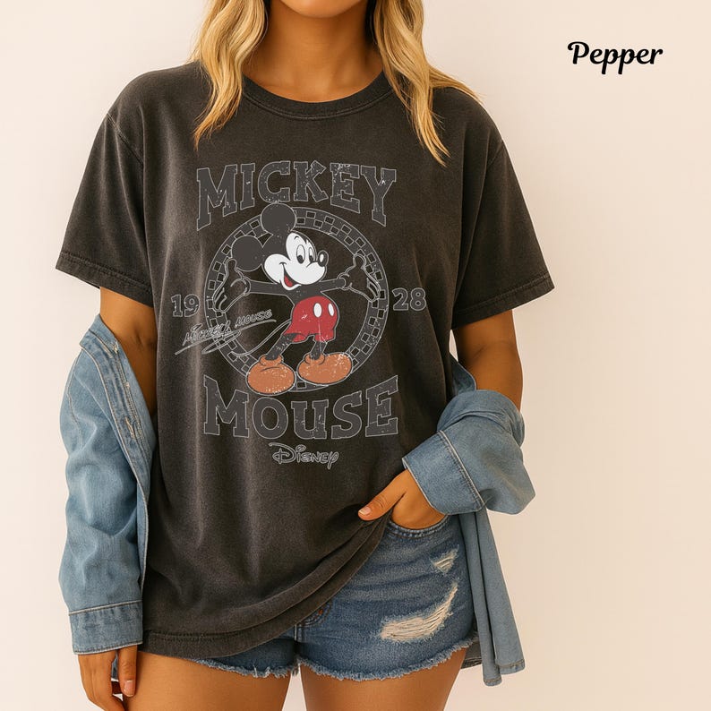 May include: Dark grey t-shirt with a distressed Mickey Mouse graphic, the text "Mickey Mouse" and "1928". The shirt has short sleeves and a crew neck. The word "Disney" is printed below the graphic.