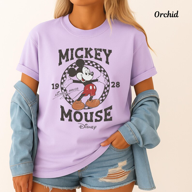 May include: Orchid-coloured t-shirt with a vintage Mickey Mouse design. The graphic includes the words "Mickey Mouse" and the year "1928". The shirt has rolled-up sleeves and is a light purple colour.