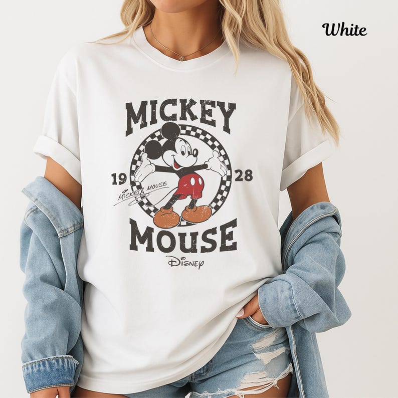 May include: White t-shirt with a distressed Mickey Mouse graphic. The design includes the text "Mickey Mouse" and the year "1928". The Disney logo is at the bottom. The shirt has short sleeves and a crew neck.