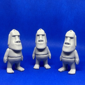 May include: Three gray, 3D printed figurines of a human-like figure with a large head and a simple, blocky body. The figures are standing on a blue surface.