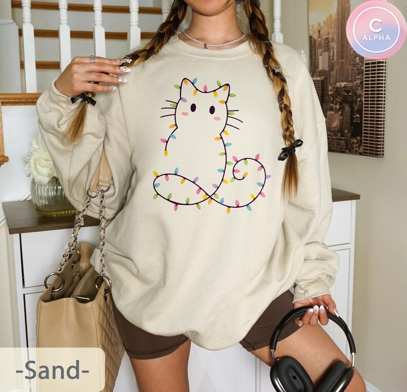 Soft sand sweatshirt with a cute cat outline wrapped in vibrant Christmas lights. Adds a gentle festive touch, ideal for cozy winter days or as a unique holiday wardrobe piece.