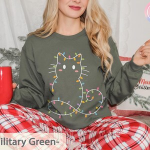 Cozy military green sweatshirt with a whimsical cat outline wrapped in colorful lights. Perfect for enjoying Christmas festivities in comfort and style.