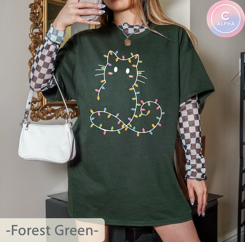 Festive forest green T-shirt with a cute cat outline decorated with Christmas lights. Ideal for holiday gatherings, bringing a subtle Christmas vibe for cat lovers.