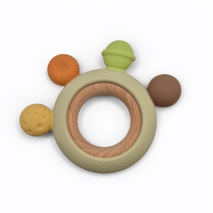 May include: A baby teether with a wooden ring center and a soft, olive green outer ring. Attached are four colorful, textured silicone shapes in orange, yellow, brown, and green. The teether is designed for infants.