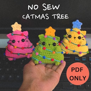 May include: Three crocheted catmas tree ornaments in pink, green, and yellow. Each ornament features a cat face with large eyes and a star on top. The ornaments are decorated with colourful lights. The text "NO SEW CATMAS TREE" is displayed above the ornaments. The text "PDF ONLY" is displayed in a red circle below the ornaments.