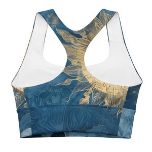 May include: A blue sports bra with a gold floral design. The bra features a racerback style with white straps and a white interior. The gold floral pattern is set against a dark blue background.