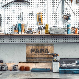Each letter in the bold word PAPA includes the silhouette of a hand tool as part of the letter.  Beneath the word PAPA is the phrase “If he can’t fix it, no one can.” The background looks like aged vertical boards similar to a flattened oak barrel. At the top and bottom are aged metal strips. This is a perfect gift for anyone’s husband, dad, stepdad, grandpa, or favorite male friend who has tools and knows who to fix things. NOTE: This is a flat metal sign, not real wood or metal.