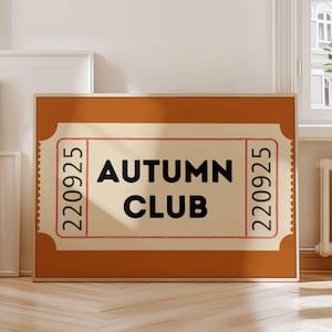 May include: A framed print featuring a ticket design with the words "AUTUMN CLUB" in bold black letters. The ticket has a beige background with red border and the numbers "220925" on each side. The frame is a warm brown color.