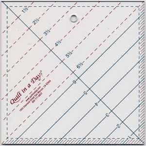 May include: A white quilting ruler with blue and red markings, featuring diagonal lines and measurements in inches. The text "Quilt in a Day" is visible. The ruler has a hole for hanging and is designed for quilting projects.