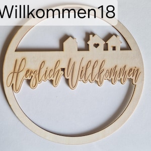 Könnte beinhalten: Ein runder Holzschild mit den Worten "Willkommen18" oben und "Herzlich Willkommen" in Schreibschrift. Das Schild zeigt eine Silhouette von Häusern und einem Herz. Das Schild ist aus hellem Holz gefertigt.