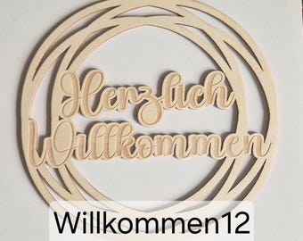 May include: A wooden circular sign with the words "Herzlich Willkommen" in a cursive font, meaning "Welcome" in German. The sign is made of light-colored wood and has a layered design. The word "Willkommen12" is printed at the bottom.