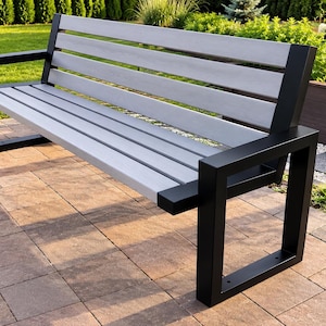 May include: A garden bench featuring a backrest and seat constructed from light gray horizontal slats. The frame is made of thick, black rectangular metal tubing that forms the armrests and legs, providing a sturdy base for the seating area.