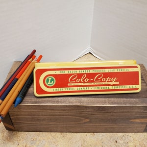 May include: A vintage tin box of Colo-Copy bonded process lead pencils. The box is yellow with red and green accents. The text on the box reads "One Dozen Bonded Process Lead Pencils Colo-Copy This Pencil is Produced in Fifteen Colors of Lead Linton Pencil Company Lewisburg, Tennessee, U.S.A."