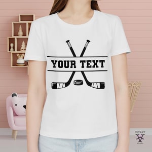 May include: White t-shirt with a black hockey stick and puck design. The text "YOUR TEXT" is printed on a black banner.