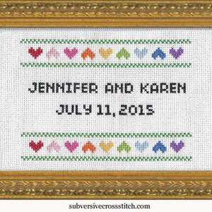 Könnte beinhalten: Ein weißer Kreuzstich-Sampler mit grünem Rand und einer Reihe bunter Herzen oben und unten. Der Text lautet "Jennifer und Karen July 11, 2015".
