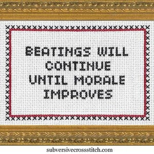 May include: Cross-stitch art in a gold frame. The text reads "BEATINGS WILL CONTINUE UNTIL MORALE IMPROVES" in black letters on a white background, with a red and black border. The website address "subversivecrossstitch.com" is at the bottom.