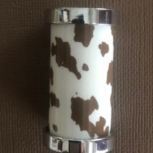 May include: A silver and white cylindrical bottle stopper with a brown cow print design.