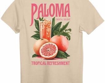 May include: A sand-coloured t-shirt with a graphic design of a Paloma cocktail, grapefruits, and leaves. The word "Paloma" is in pink script above the cocktail, with "Cocktail Delight" below it. "Tropical Refreshment" is printed below the fruit.