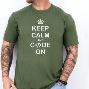 Könnte beinhalten: Olivgrünes T-Shirt mit dem weißen Text "KEEP CALM AND CODE ON" und einer kleinen Krone. Das kurzärmelige Oberteil hat einen Rundhalsausschnitt. Der Text ist mittig auf der Vorderseite des Shirts platziert.