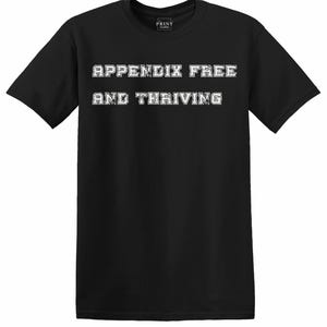May include: A black short-sleeved t-shirt featuring the white text "APPENDIX FREE AND THRIVING" printed in a bold, block-style font across the chest. The garment has a crew neckline and a standard fit, with a small brand label inside the collar.