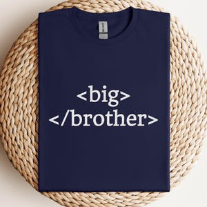 Puede incluir: Camiseta azul marino con el texto blanco "<big> /brother>". La camiseta se muestra sobre una superficie redonda y tejida. La esquina superior izquierda tiene un logotipo que dice "The Print Studio" y "Worldwide Shipping".