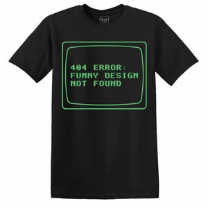 May include: Black t-shirt with a green-outlined rectangle displaying the text "404 ERROR: FUNNY DESIGN NOT FOUND" in a retro computer font. The shirt is a crew neck style and has short sleeves. The Print Studio logo is in the upper left corner.