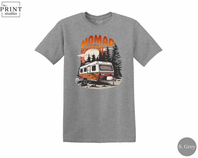 May include: A heather grey t-shirt featuring a graphic of a vintage camper in a forest scene with the text "NOMAD ADVENTURE". The design includes a sunset and pine trees, creating a nature-inspired theme.