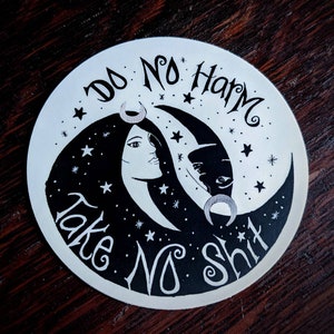 May include: Black and white sticker featuring a crescent moon design. The moon is split into two halves, one with a woman's face and the other with a cat's face. The text "Do No Harm Take No Shit" is written around the moon.