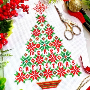 Può includere: Un disegno a punto croce di un albero di Natale su tessuto bianco. L'albero è decorato con motivi rossi e verdi a forma di fiocco di neve e le parole "MERRY CHRISTMAS". Forbici dorate e filo da ricamo rosso sono nelle vicinanze.