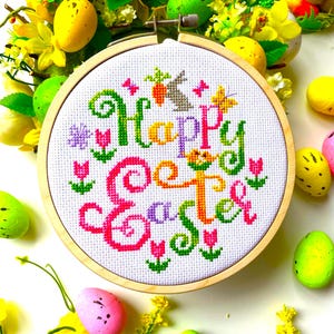 May include: A white embroidery hoop with a colorful cross-stitch design that says "Happy Easter" surrounded by yellow, green, and pink Easter eggs and flowers.