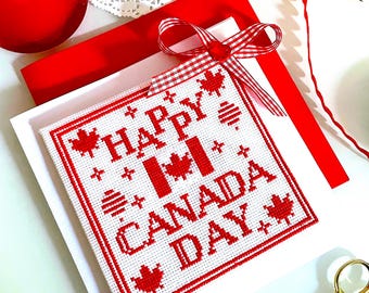 Puede incluir: Una tarjeta bordada con la frase "HAPPY CANADA DAY" en rojo sobre fondo blanco. La tarjeta presenta diseños de hojas de arce y una cinta a cuadros roja y blanca. Otros elementos incluyen hilo rojo, tijeras y un sobre rojo.