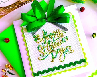 Könnte beinhalten: Eine handgefertigte St. Patrick's Day-Karte mit einem grünen, gewellten Rand und einer großen grünen Schleife. Die Karte zeigt Kreuzstich-Stickerei mit den Worten "Happy St. Patrick's Day" in grüner und goldener Farbe. Bastelbedarf wie Schere, Band und Faden.