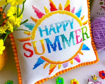 May include: A white pillow with a colorful embroidered sun and the text "HAPPY SUMMER". The pillow has a bright orange pom-pom trim.