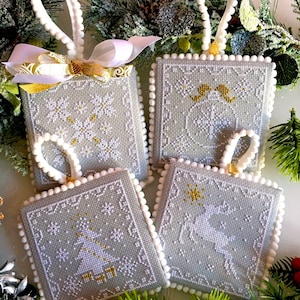 Könnte beinhalten: Vier graue und weiße Weihnachtsornamente mit weißem Bommelbesatz. Jedes Ornament zeigt eine andere Winterszene mit goldenen Akzenten. Die Ornamente sind mit Schneeflocken, einem Weihnachtsbaum, einem Rentier und einem Engelpaar verziert.