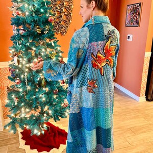 May include: A long, blue quilted robe with a gold fish embroidered on the back. The robe is made of patchwork fabric and has a collar.