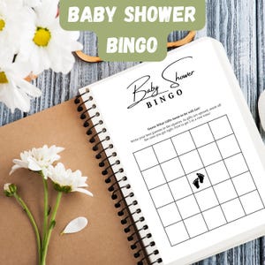 Könnte beinhalten: Ein Baby Shower Bingo-Spielbuch mit Spiralbindung, mit den Worten "Baby Shower Bingo". Das Spiel enthält Quadrate zum Erraten von Geschenken, mit Anweisungen. Weiße Blumen und ein Holzring sind im Hintergrund.