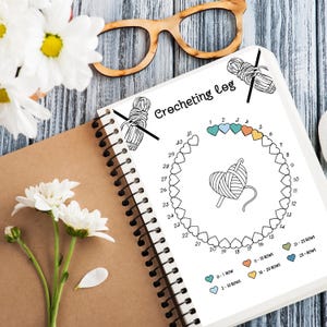 May include: A crocheting log with a circle of hearts to track progress. The hearts are color-coded to indicate the number of rows completed. The colors are teal, light blue, orange, and yellow. The log also includes a drawing of a crochet hook and yarn.