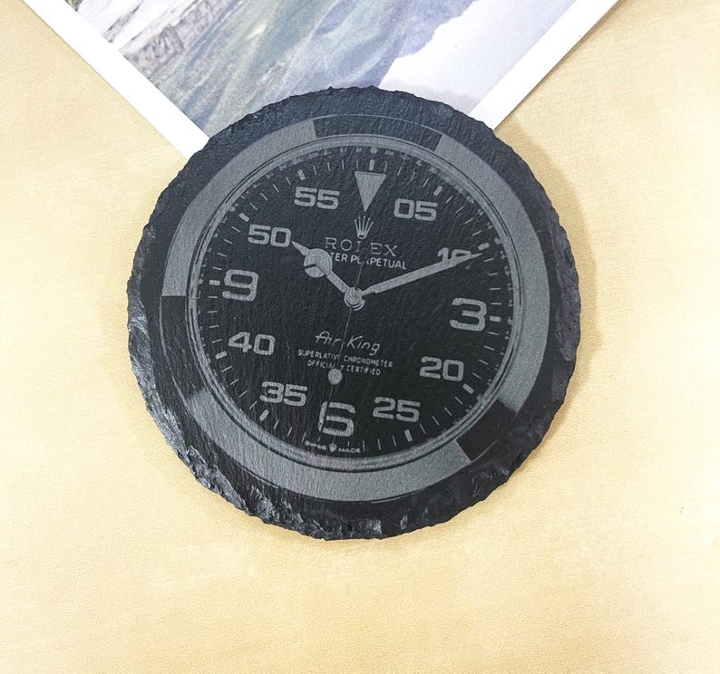 K&ouml;nnte beinhalten: Schwarzer Schieferuntersetzer mit einem lasergravierten Rolex Air-King-Zifferblatt. Das Zifferblatt der Uhr verf&uuml;gt &uuml;ber wei&szlig;e Markierungen und den Text "ROLEX OYSTER PERPETUAL" und "Air-King SUPERLATIVE CHRONOMETER OFFICIALLY CERTIFIED".