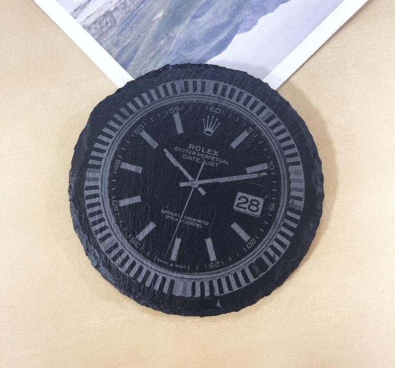 K&ouml;nnte beinhalten: Schwarzer Schieferuntersetzer mit einem lasergravierten Rolex-Zifferblatt. Das Zifferblatt zeigt den Text "Rolex Oyster Perpetual Datejust" und das Datum "28".