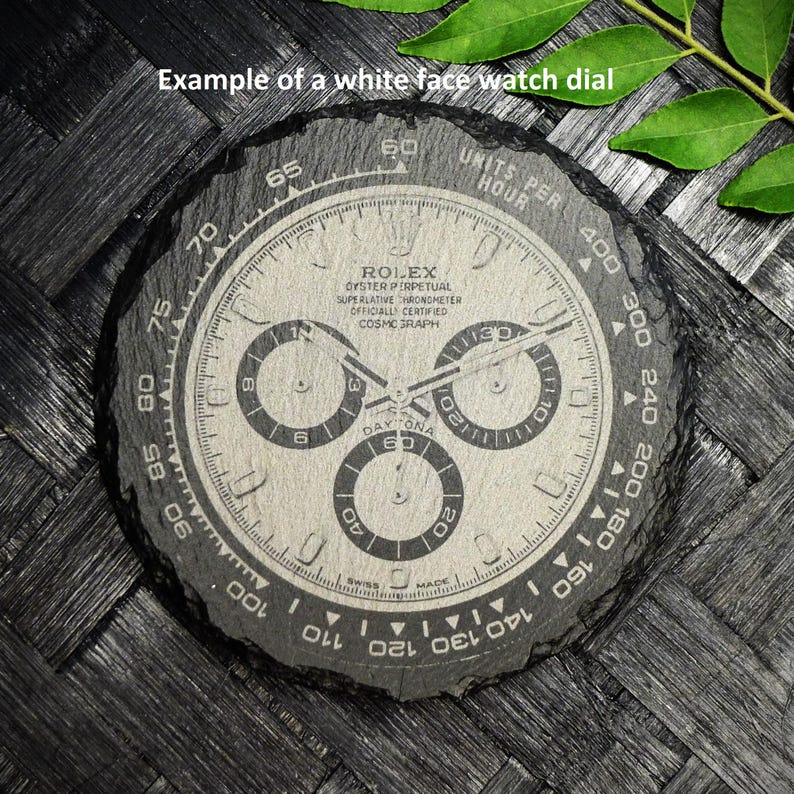 K&ouml;nnte beinhalten: Ein wei&szlig;es Zifferblatt mit schwarzen Markierungen und dem Text "ROLEX OYSTER PERPETUAL SUPERLATIVE CHRONOMETER OFFICIALLY CERTIFIED COSMIC GRAPH DAY-TONA".