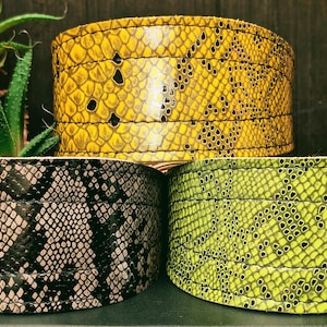 May include: Three leather collars with a snake skin pattern. The collars are in yellow, green, and black and gray.